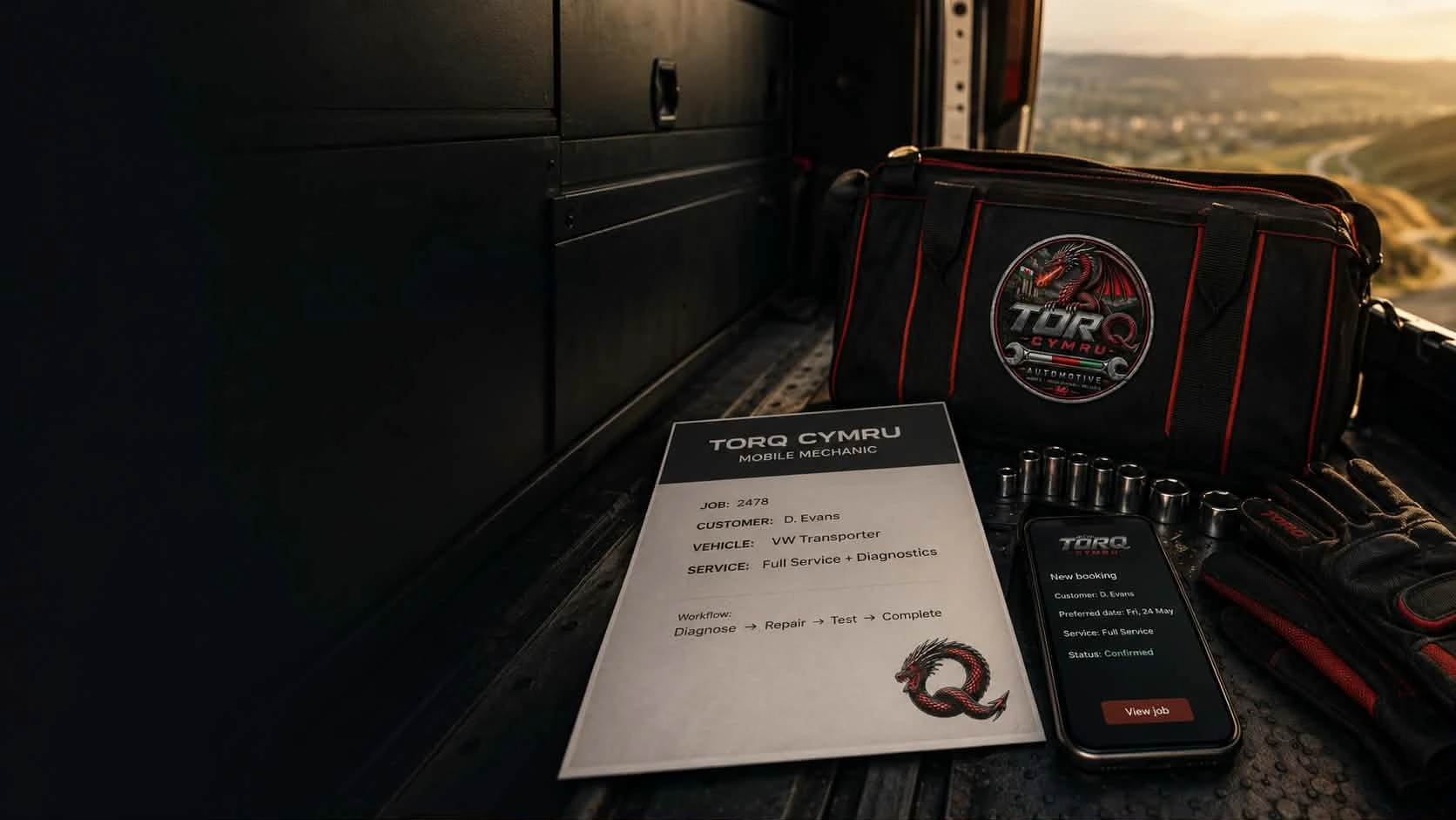 Inside a dark TorQ Cymru service van, with black cabinetry on the left and a branded bag, job sheet, phone booking screen and tools on the right, with the South Wales landscape beyond